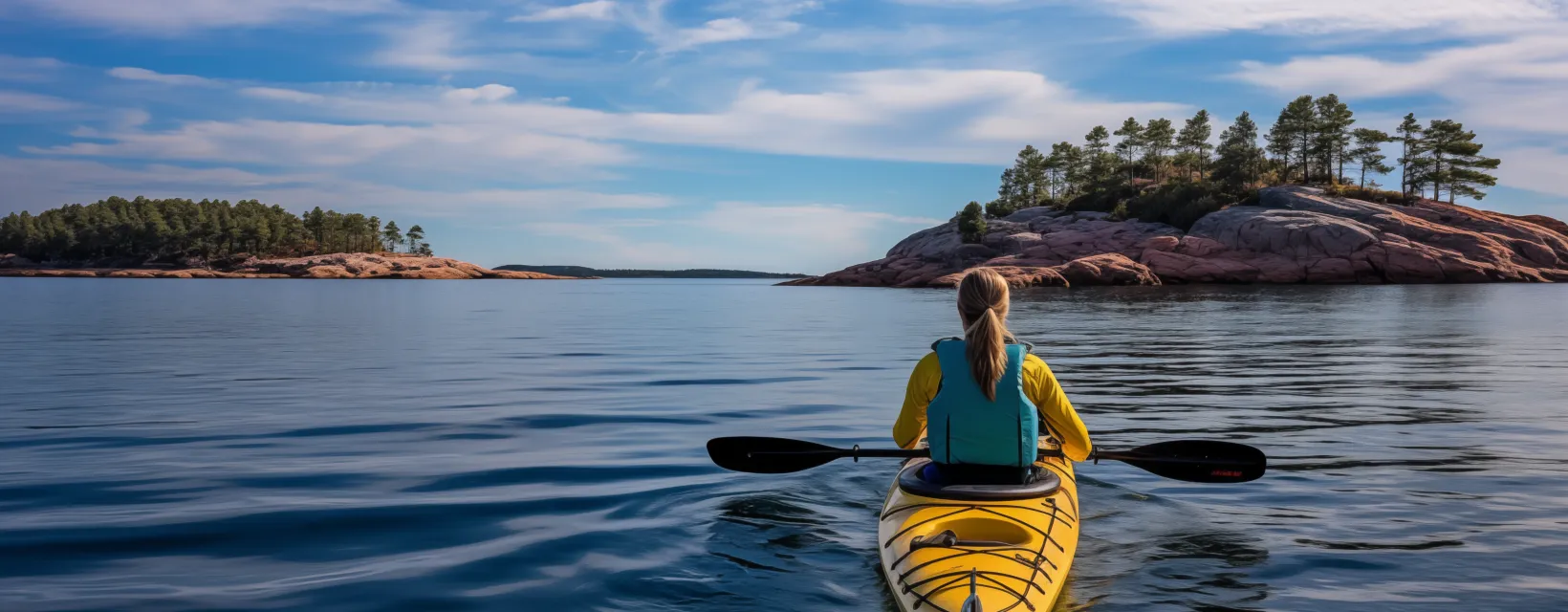 AI-genererad bild av ryggen på en kvinna som sitter i en gul kajak i ett skärgårdslandskap som liknar Åland.