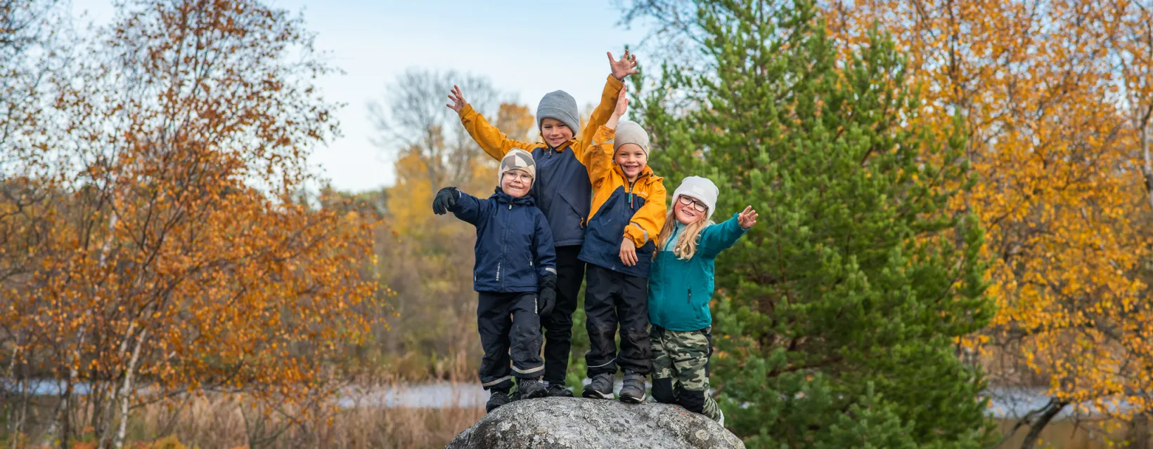 Fyra höstklädda barn som klättrat upp på en sten och vinkar.