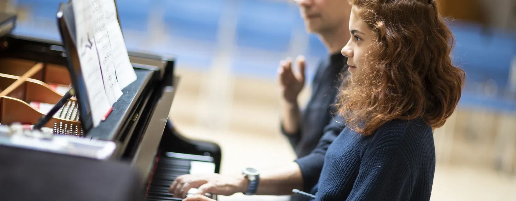 Flicka sitter och spelar piano tillsammans med sin pianolärare.