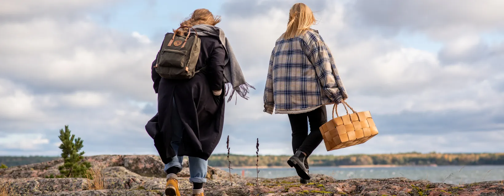 Ryggen på två kvinnor som går mot havet över klipporna i skärgården en höstdag.