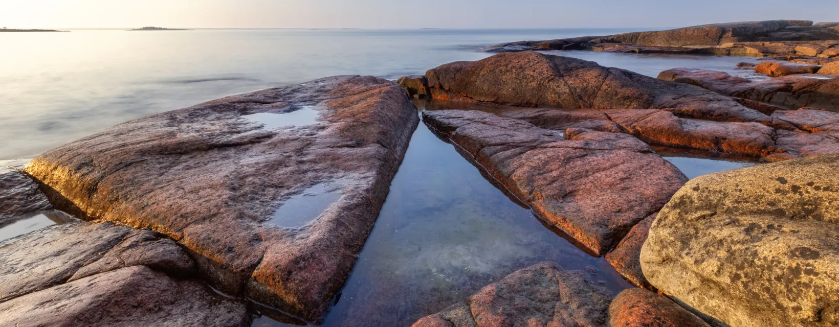 Vacker tidig solig morgon på granitröda klippor vid blankt hav på Åland.