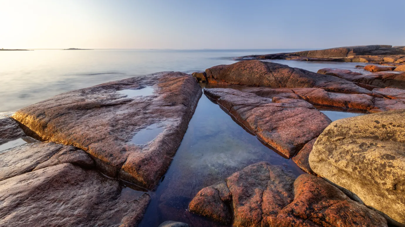 Vacker tidig solig morgon på granitröda klippor vid blankt hav på Åland.