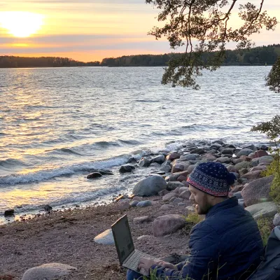 Man sitter vid havet på Åland och jobbar på distans med sin bärbara dator.