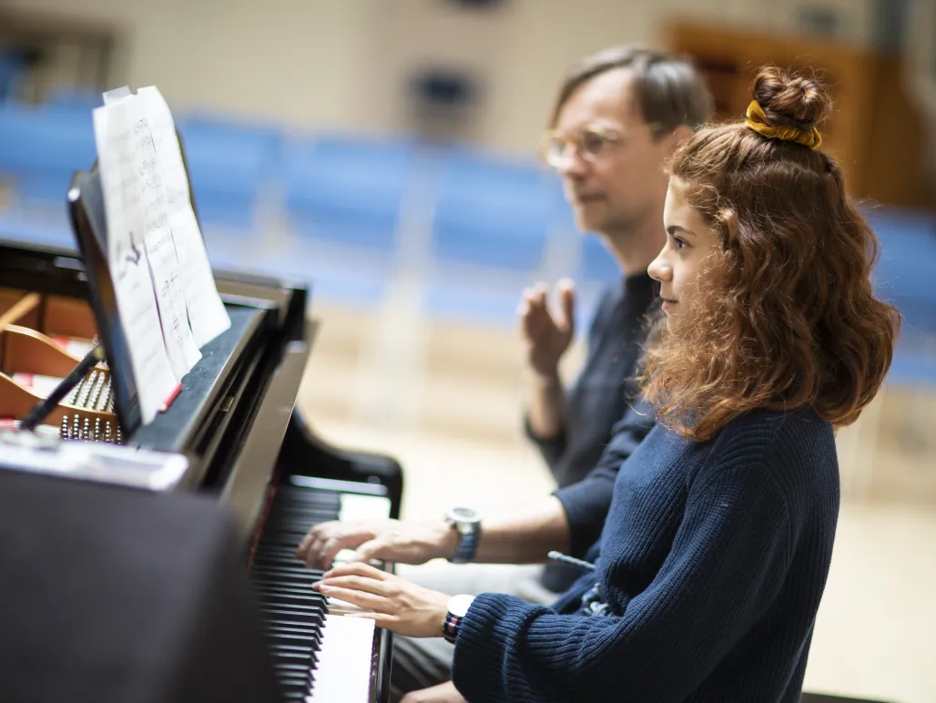 Flicka sitter och spelar piano tillsammans med sin pianolärare.